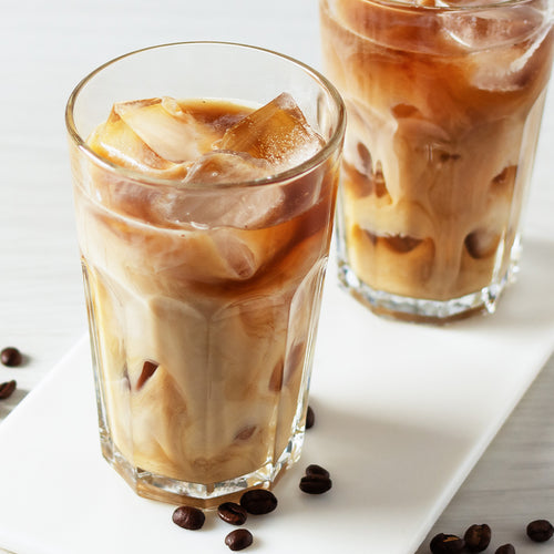 Two Thai iced coffees in tall clear glasses on a white plate.