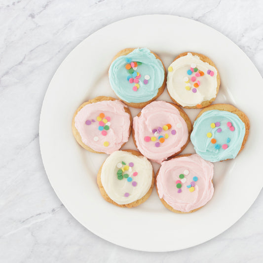 Top down view of a plate of sugar cookies topped with icing and sprinkles on a marble countertop.