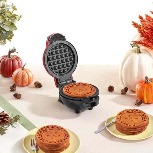 Three square mini pumpkin-flavored waffles with a Jack-O-Lantern print on a white plate with a scoop of vanilla ice cream and syrup.
