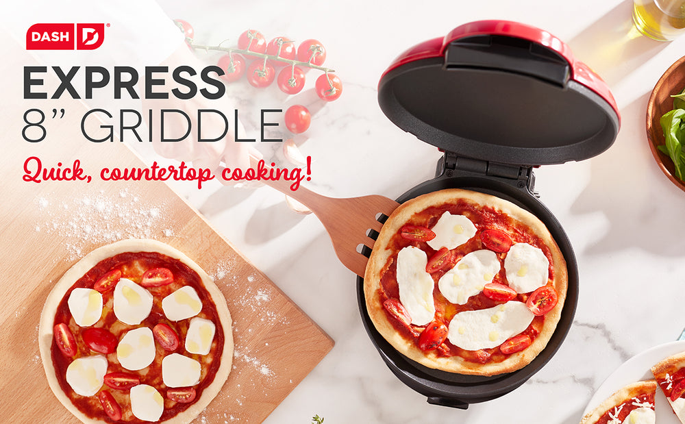 A pizza in a red 8 inch Express Griddle for quick countertop cooking.