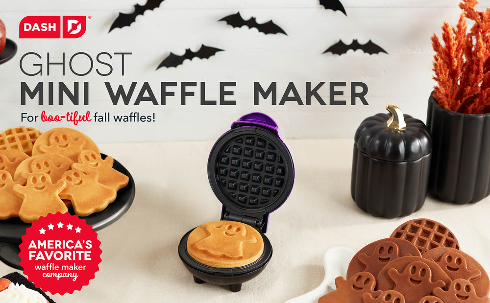 The Dash Ghost Mini Waffle Maker on a white table cloth next to halloween decorations and ghost waffles.