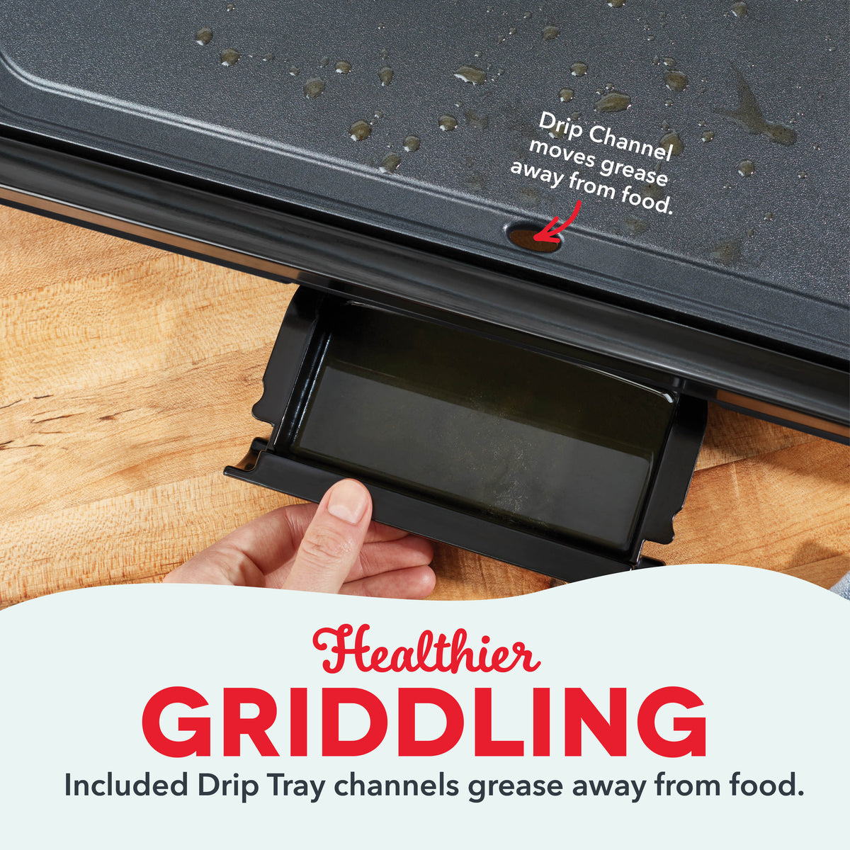 Black griddle with gray nonstick surface and removable drip tray being pulled out by hand on wooden surface.