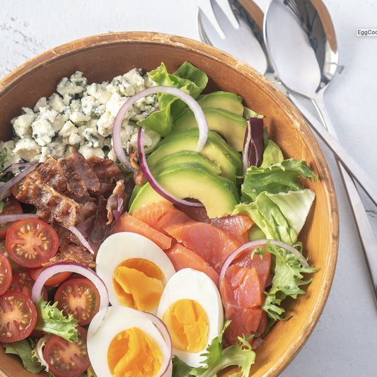 A cobb salad with hardboiled eggs, bacon, avocado, tomato, and blue cheese in a wood bowl.