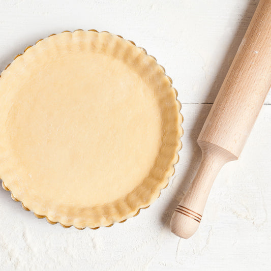 A rolling pin sitting next to a pie dish filled with pie crust.