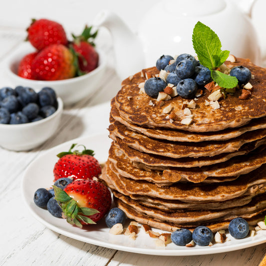 A plate of protein pancakes topped with blueberries and strawberries.