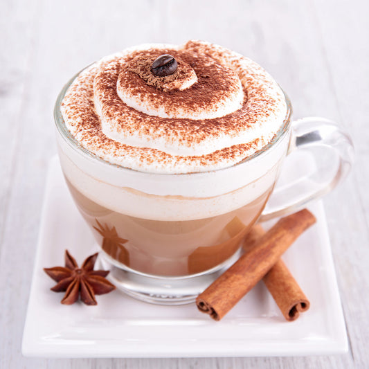 Cinnamon mocha coffee in a glass mug topped with whipped cream and cinnamon on a white plate.