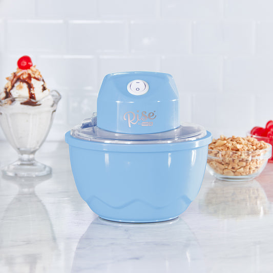 The Rise by Dash Personal Ice Cream Maker sits on a marble counter next to an ice cream sundae.