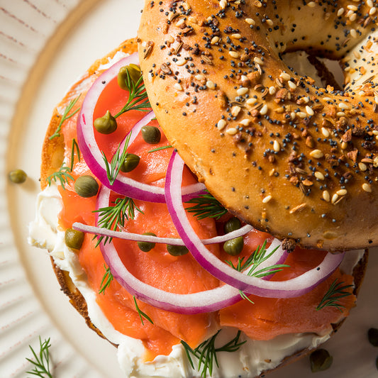 An everything bagel with cream cheese, salmon, capers, red onions, and dill on a white plate.