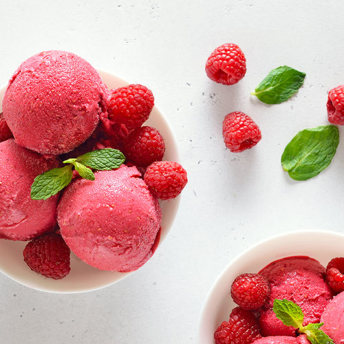 Three scoops of raspberry frozen yogurt in a white bowl with raspberries.