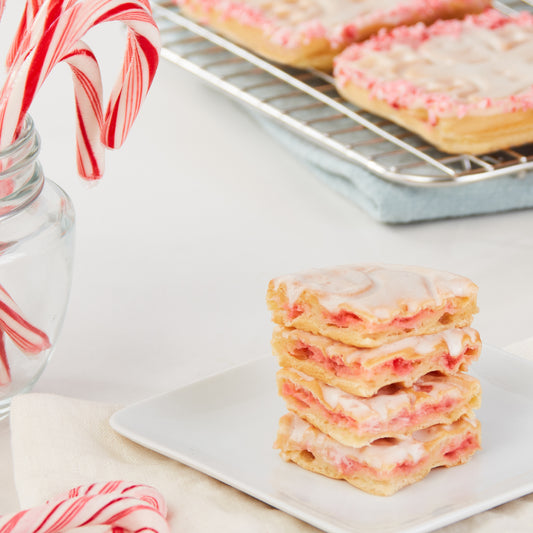 Four peppermint waffles stacked on a white plate next to candy canes.