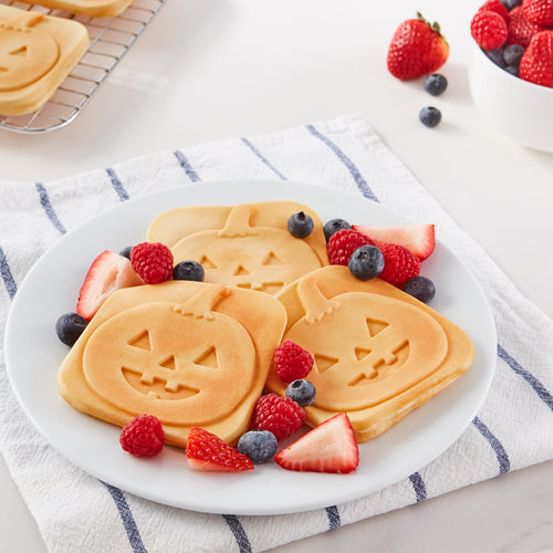 Three square mini waffles with a Jack-O-Lantern print on a white plate with berries.