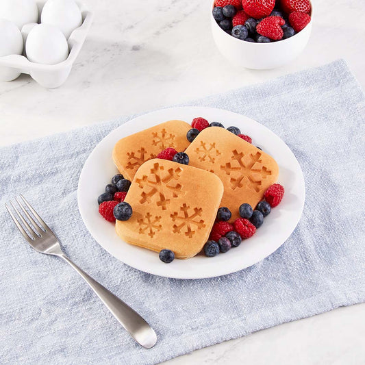 Three mini waffles with a snowflake print on a white plate with strawberries and blueberries.