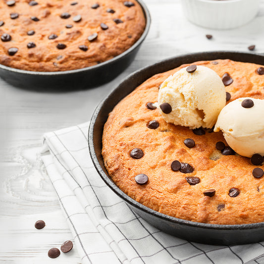 Two large chocolate chip skillet cookies in a skillet on a linen cloth.