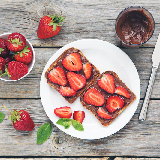Two pieces of toast with Nutella spread and strawberries on top on a white plate.