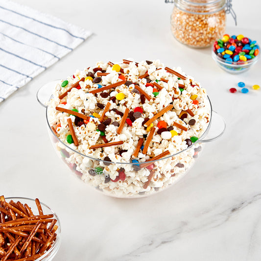 A clear bowl filled with popcorn, M&Ms candy, pretzel sticks and marshmellows.