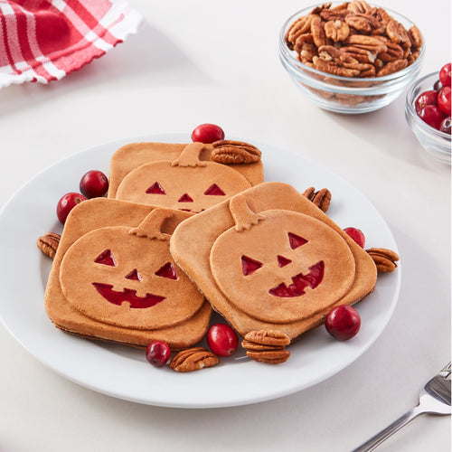 Three square mini waffles with a Jack-O-Lantern print on a white plate with pecans and cranberries.
