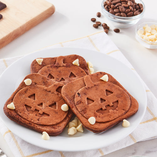 Three square mini chocolate waffles with a Jack-O-Lantern print on a white plate with white chocolate chips.