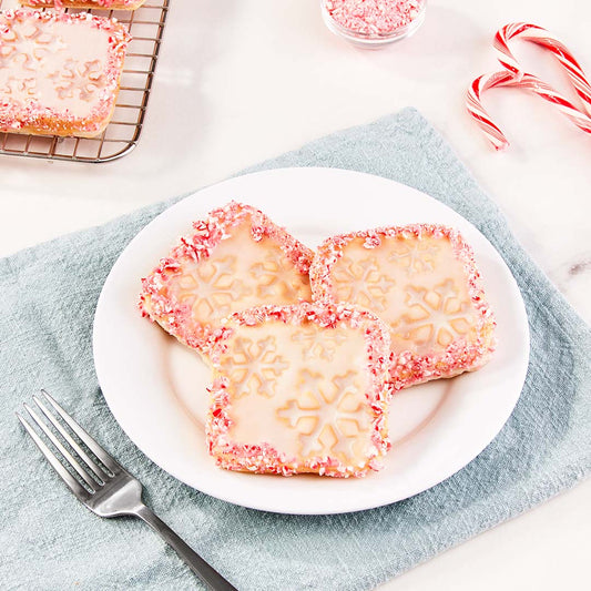 Three mini waffles with a snowflake print topped with a peppermint glaze on a white plate.