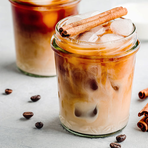 Iced vanilla latte in a clear glass topped with a cinnamon stick.