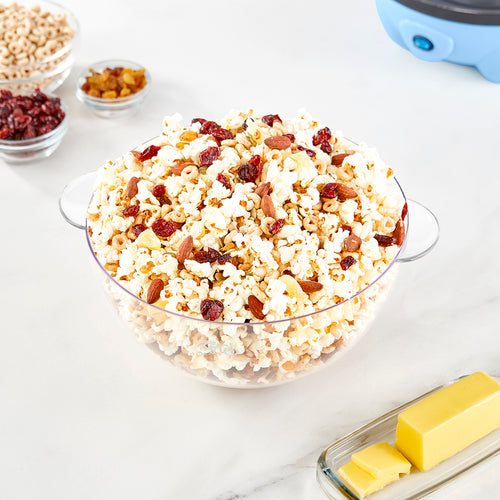 A clear bowl filled with popcorn, almonds, cranberries, and sunflower seeds.