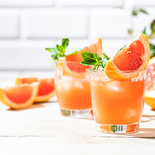 Two short glasses filled with a pink drink topped with a grapefruit wedge and mint.