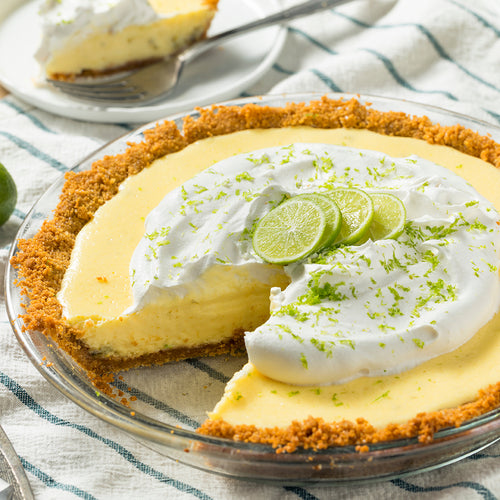 A Key Lime Pie in a clear pie dish with one slice removed.