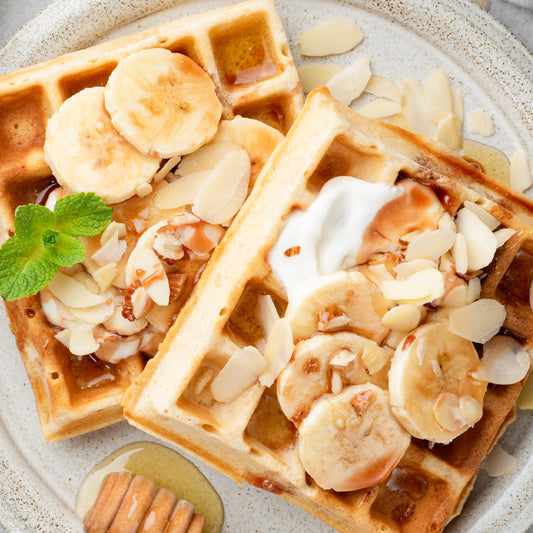 Banana bread waffles topped with banana slices, sliced almonds, and honey.