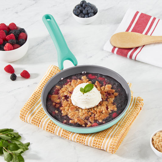 A berry crisp in a pan topped with cinnamon and oats crumble and a scoop of ice cream