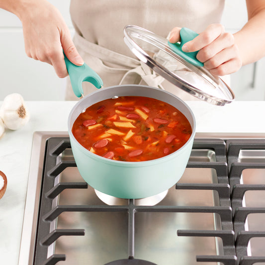 A man is holding pot of soup and lid on a stove burner.