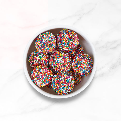 A stack of Confetti Donut Bites in a white bowl on a marble countertop.