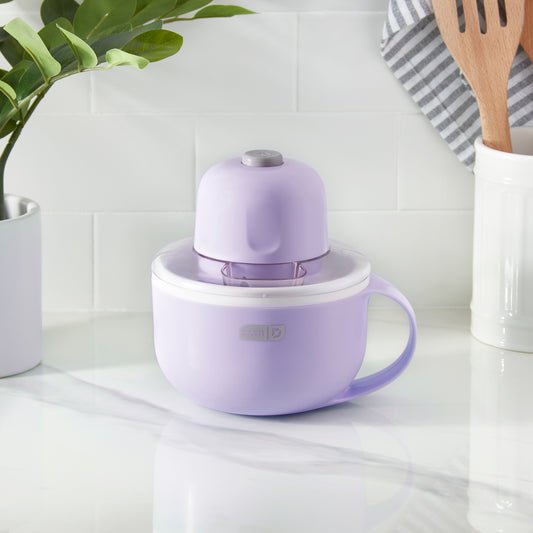 The Rise by Dash Personal Ice Cream Maker sits on a marble counter next to an ice cream sundae.