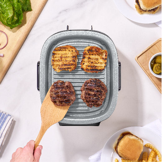 3QT Flip & Fry™ Digital 2-in-1 Grill + Air Fryer Air Fryer Dash Forged Iron grill with grilled patties and a wooden spatula on a table with burger ingredients.