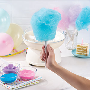 Cotton candy machine with blue cotton candy, surrounded by colorful balloons and a cake.