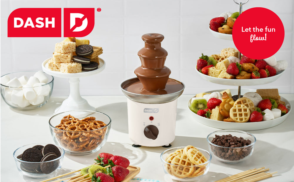Chocolate fountain with snacks and fruits on a white surface, featuring the Dash brand.