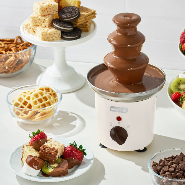 Chocolate fountain with assorted treats on a white surface