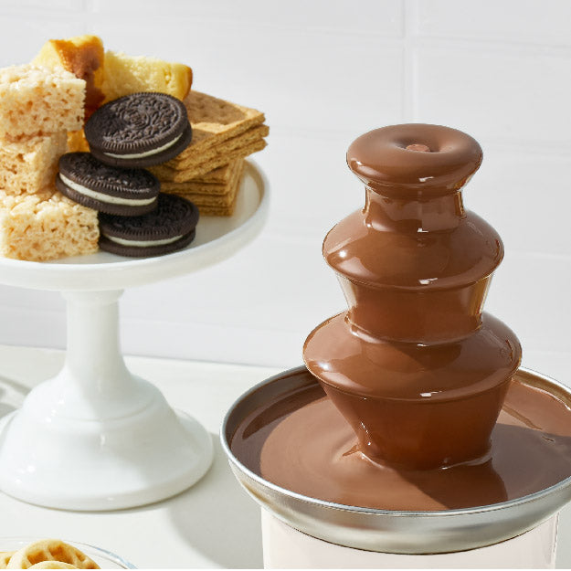 Chocolate fountain with a variety of snacks on a white background
