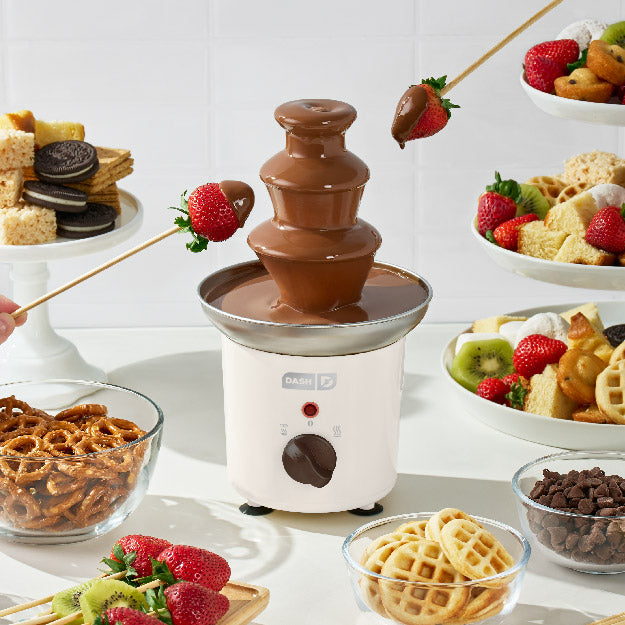 Chocolate fondue fountain with various dipping items on a table