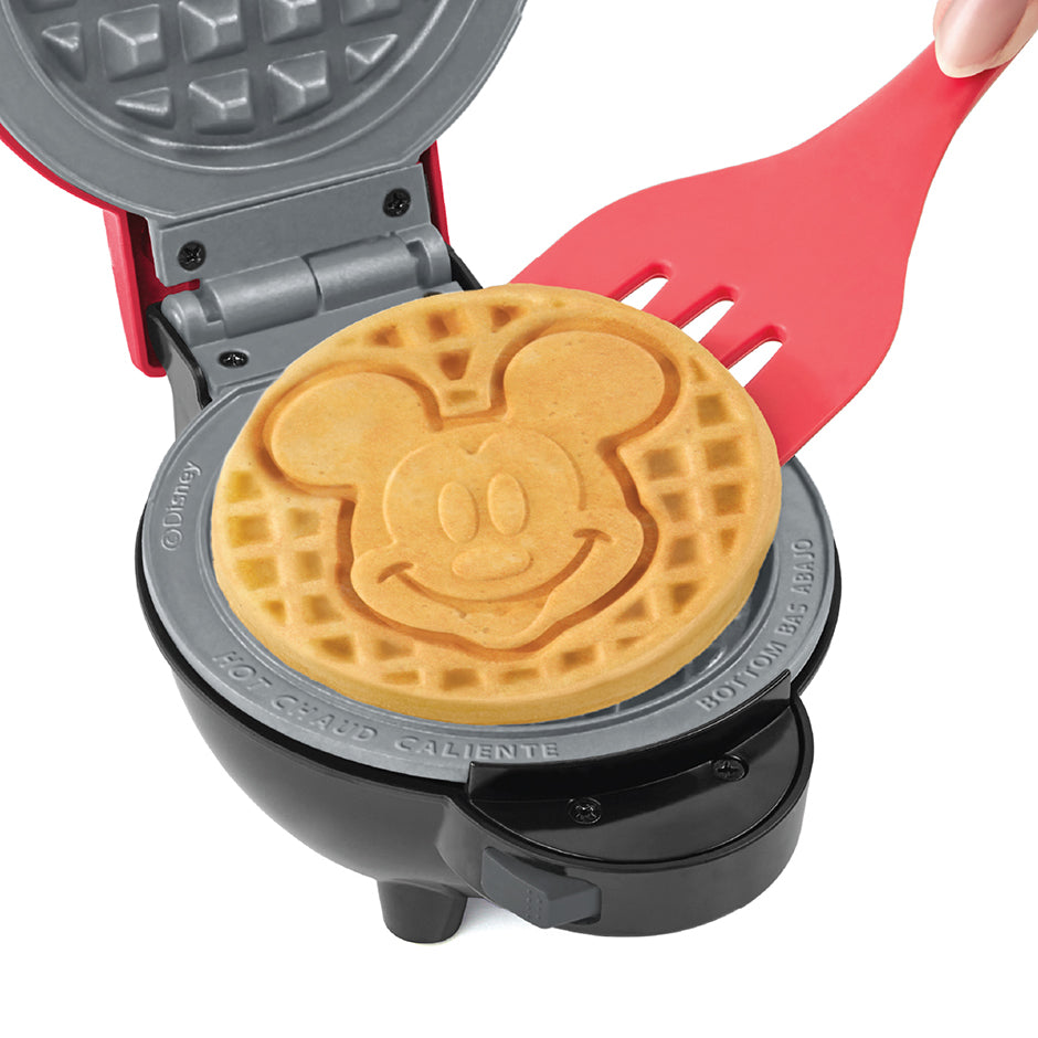 Fresh golden Mickey Mouse waffle cooked in the Dash | Disney MultiMaker™ Mini System, ready to serve with a spatula.