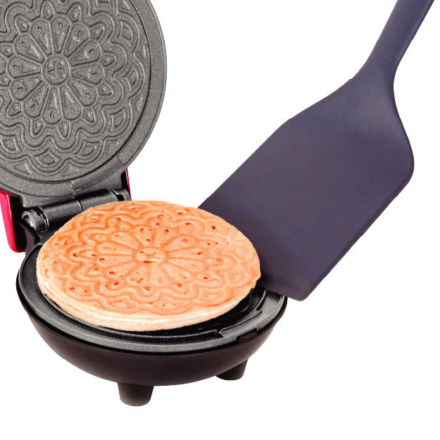 Golden pizzelle cookie lifting off the Dash Mini Pizzelle Maker with included spatula.