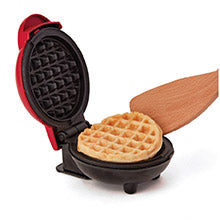 Mini waffle maker with a cooked waffle and wooden spatula on a white background