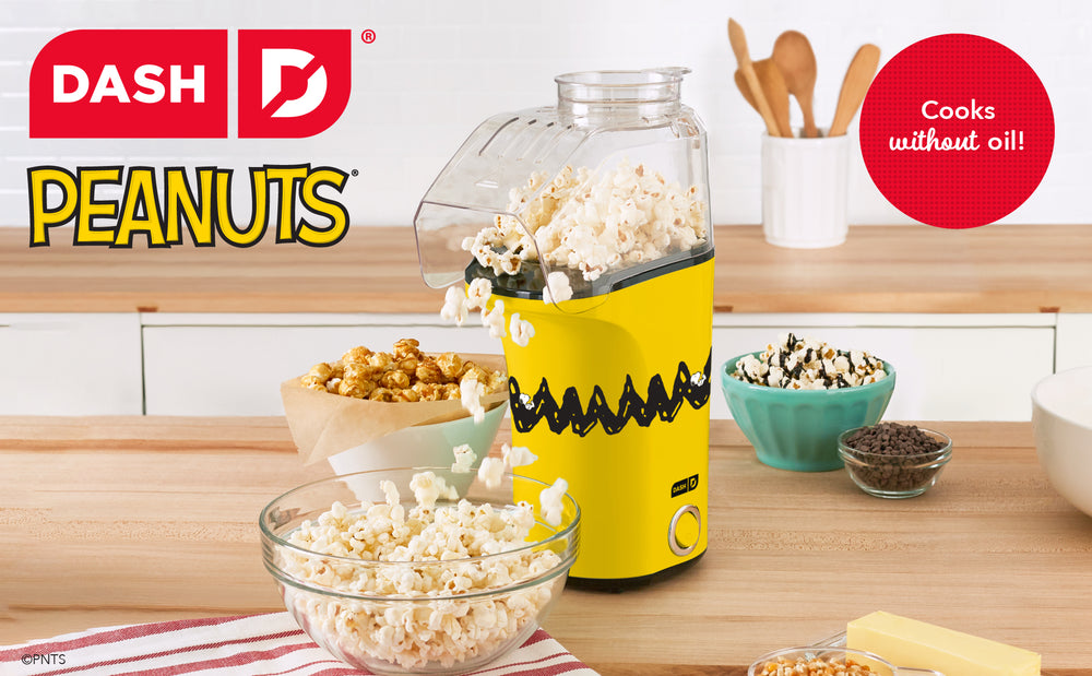 Peanuts® x Dash  Popcorn Maker in yellow Charlie Brown design popping oil-free popcorn in kitchen.