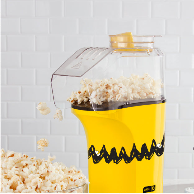 Peanuts® x Dash Popcorn Maker popping fresh popcorn in yellow Charlie Brown design.