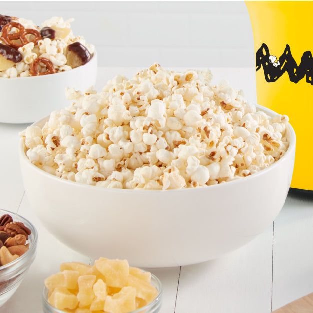 Bowl of freshly popped popcorn beside the yellow Peanuts® x Dash Popcorn Maker.