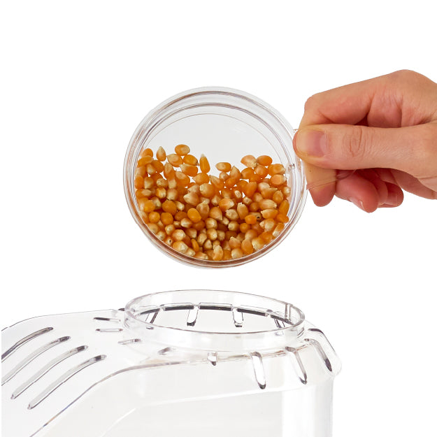 Hand pouring popcorn kernels into the top of the Peanuts® x Dash Popcorn Maker.