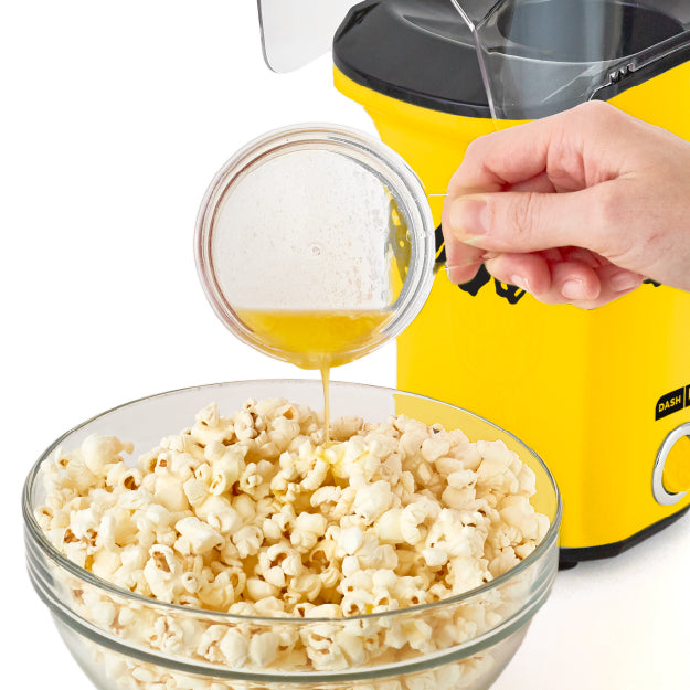 Hand pouring melted butter over fresh popcorn made with Peanuts® x Dash Popcorn Maker.