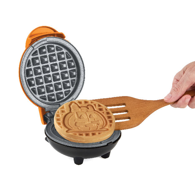 Waffle maker with a Snoopy design waffle and a wooden spatula on a white background