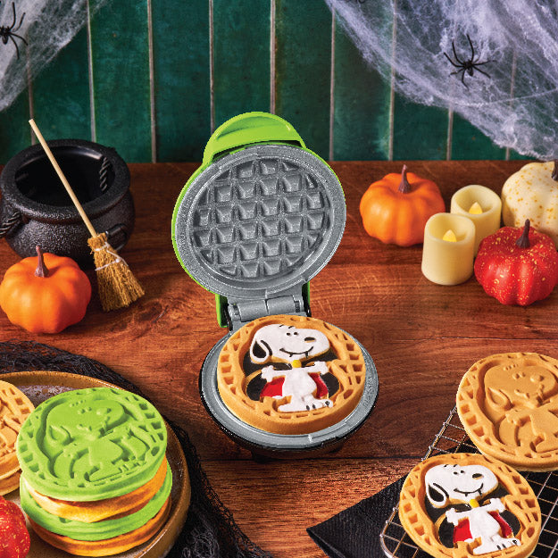 Halloween-themed waffle maker with vampire Snoopy character on a wooden table with decorative items.