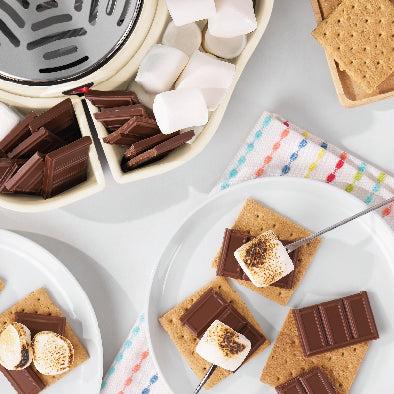 S'mores ingredients including graham crackers, chocolate bars, and marshmallows on a white surface.