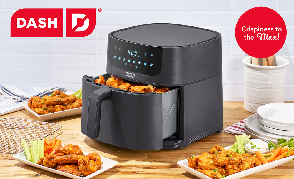 Black air fryer with plates of food on a wooden table, featuring the Dash brand.