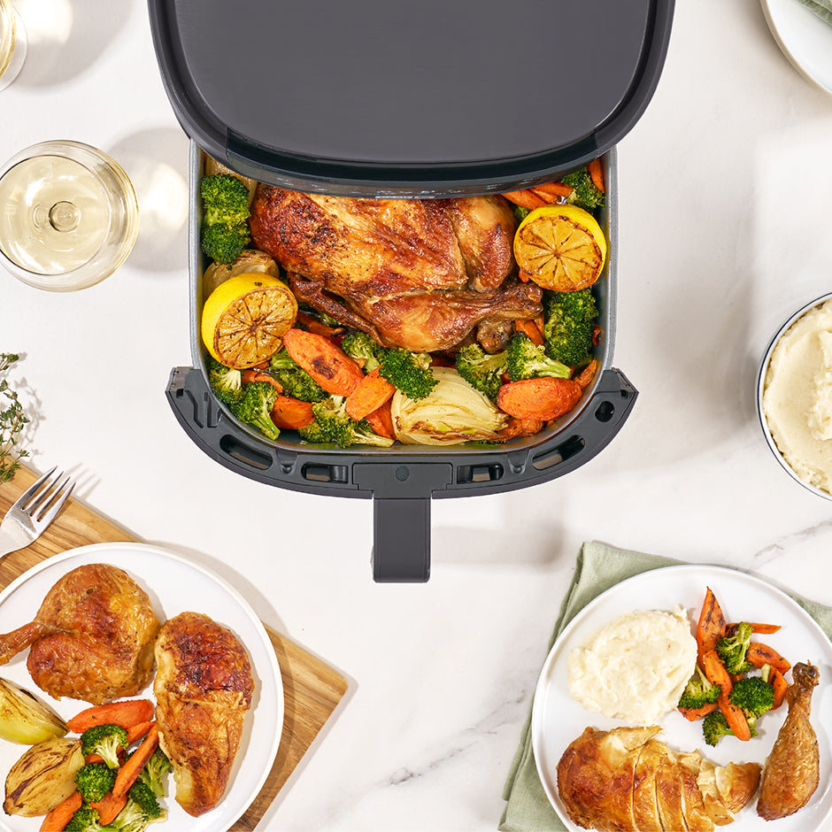 Air fryer with roasted chicken and vegetables on a dining table with plates of food.